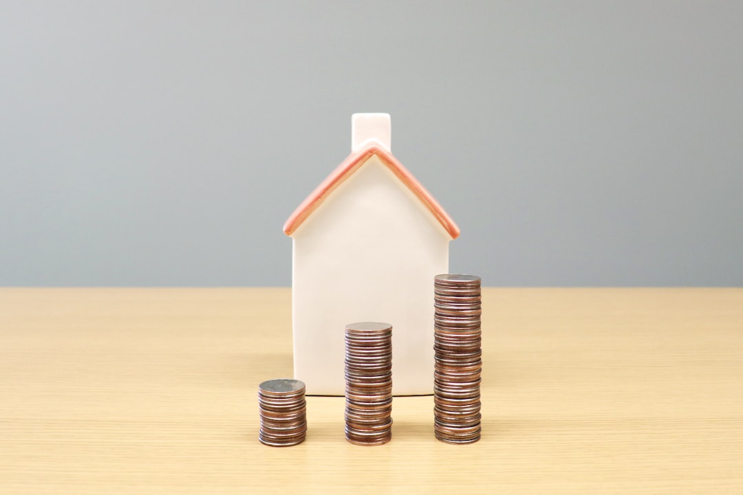 Piggy bank shaped like a house with stacks of coins beside it on a wooden table